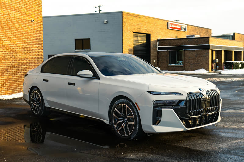 BMW paint protection film: white BMW 7 Series sedan in front of a brick building