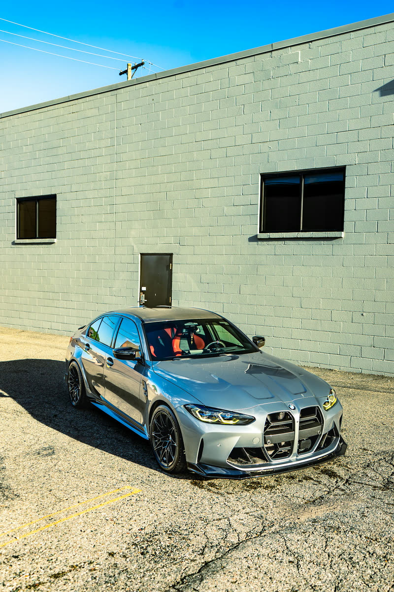 Grey BMW M3 on an asphalt lot in front of a block wall