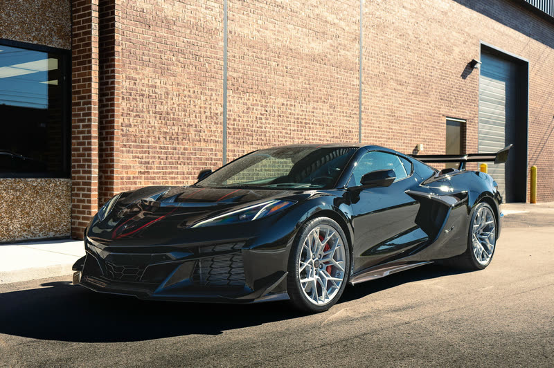 Black Corvette Z06 with red hood stripes in front of a brick wall