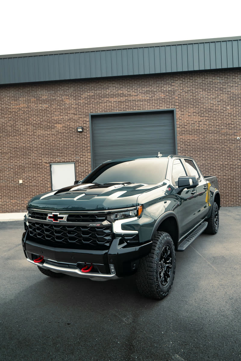 Dark green Chevrolet Silverado pickup in front of a brick building